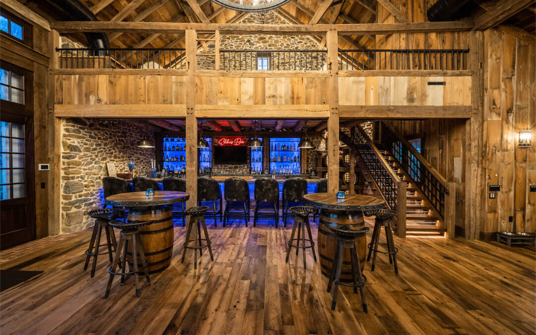 A room with reclaimed hardwood floors, barrel tables, and a counter in the back.