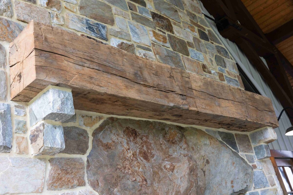 A wooden mantel shows long checks running down the side as it sits against a stone wall.