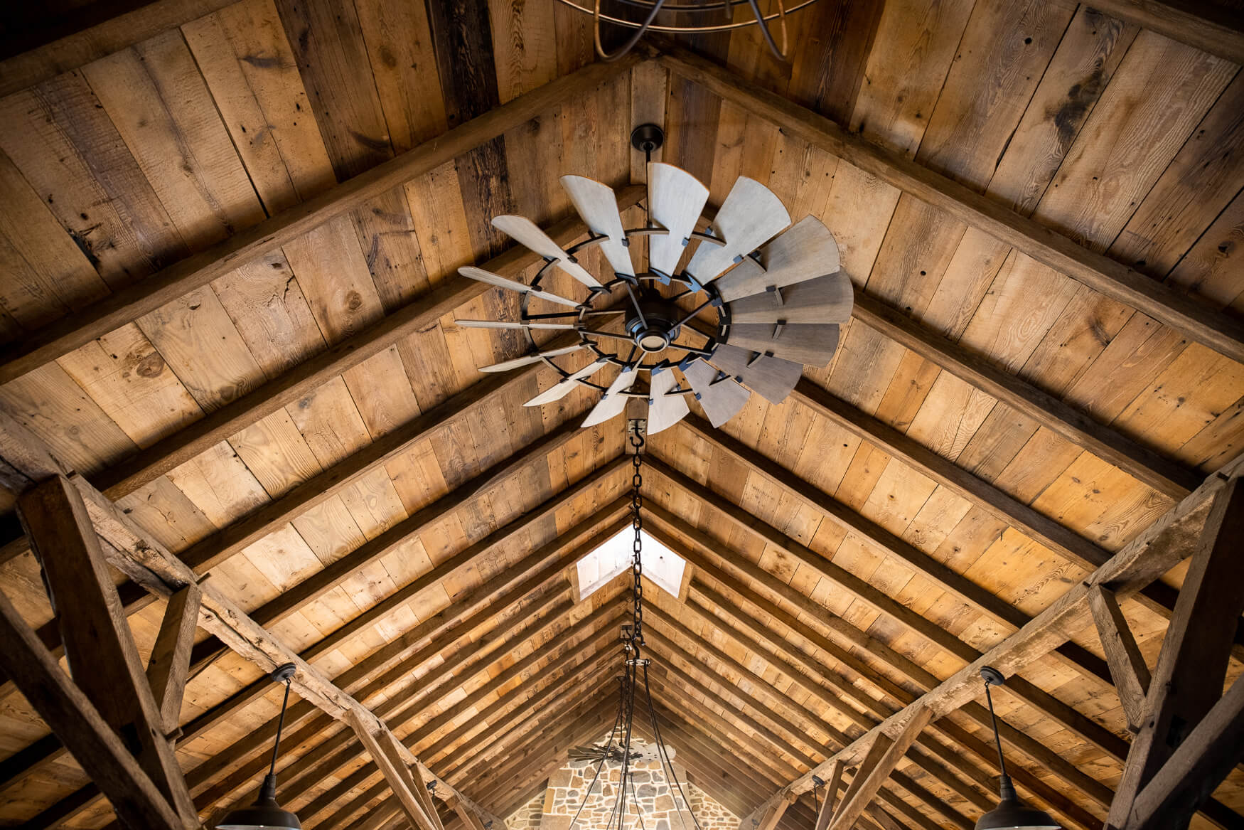 Reclaimed wood box beams along the ceiling of a building with a fan spinning below them